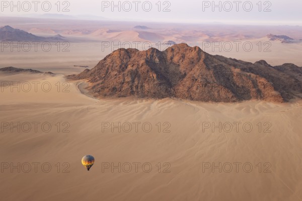 The hot-air balloon above an arid plain and isolated mountain ridges at the edge of the Namib