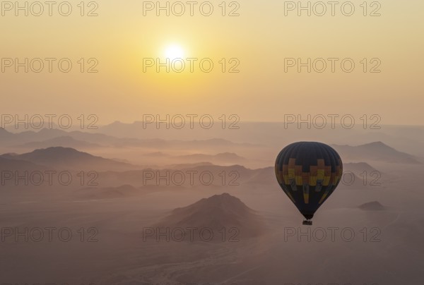 The hot-air balloon above an arid plain and isolated mountain ridges at the edge of the Namib