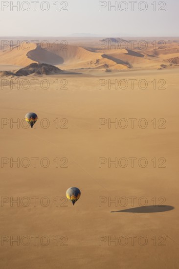 Two hot-air balloons above an arid plain at the edge of the Namib Desert. Aerial view from another