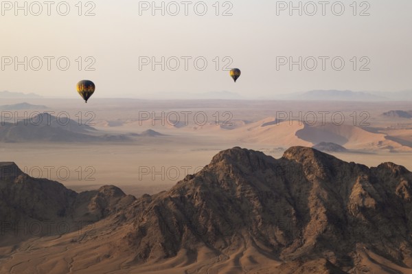 Two hot-air balloons above an arid plain and isolated mountain ridges at the edge of the Namib
