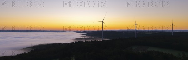Row of wind turbines along the horizon at sunrise with fog in the distance, near Schorndorf,