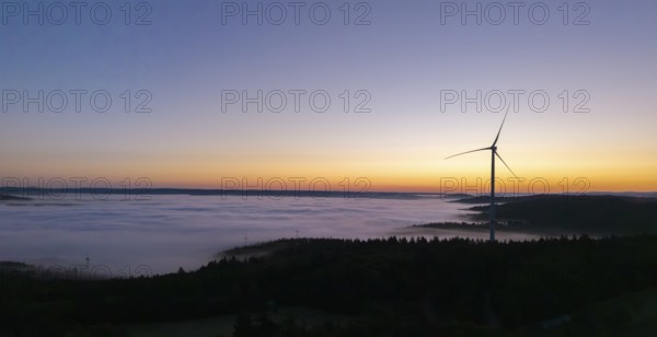 Single wind turbine above a sea of fog against a colourful morning sky, near Schorndorf, Remstal,