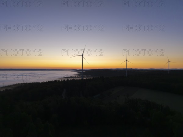 Three wind turbines in front of an orange and blue sky at sunrise with fog, near Schorndorf,