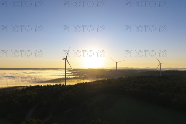 Three wind turbines in the soft morning light over a misty forest landscape, near Schorndorf,