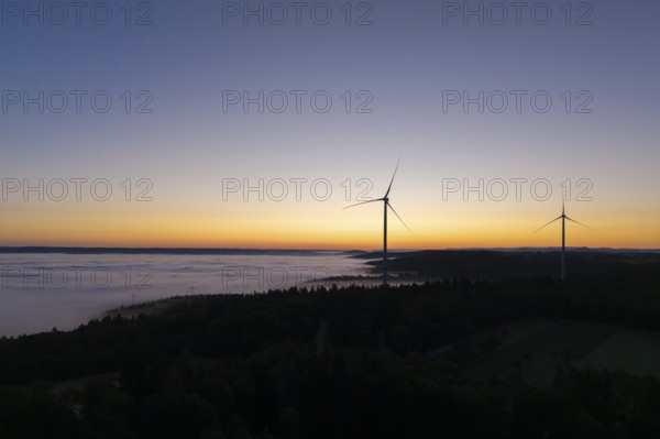 Two wind turbines in front of a colourful sunrise sky with fog over the landscape, near Schorndorf,