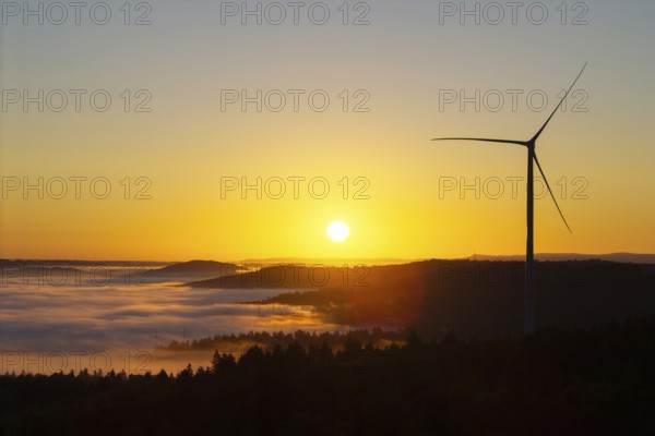 A wind turbine rises into the sunrise sky above misty hills, near Schorndorf, Rems-Murr district,