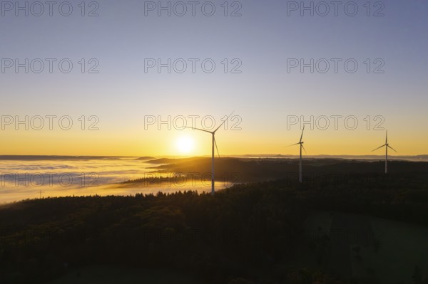 Three wind turbines overlook a fog-covered forest at sunrise, near Schorndorf, Rems-Murr district,