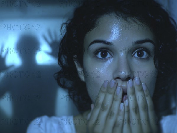 A woman gripped by fear, behind her an eerie silhouette of a shadow, symbolic image for anxiety