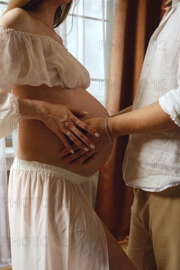A pregnant woman in a soft dress enjoys a loving moment with her partner. They are inside a cozy