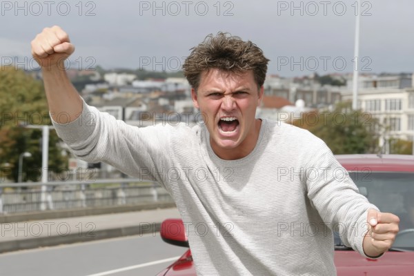 A man shouts angrily with clenched fists on a road, symbolic image for aggressive behaviour in road