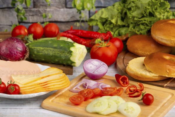 Bagels alongside sausage, cheese and fresh vegetables such as tomatoes, lettuce, cucumber and