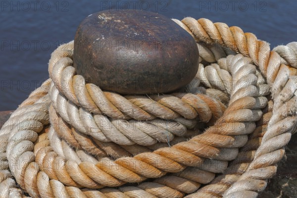 Ropes knotted around a metal bollard, beige and brown, rich in contrast against a dark blue
