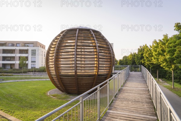 Wooden spherical structure in front of modern residential building at sunset in urban park, small