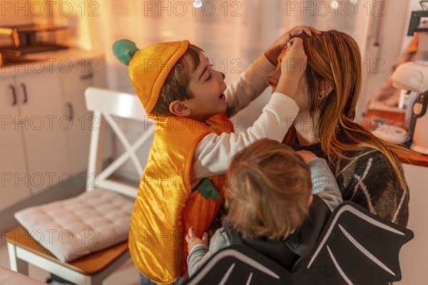 Two brothers, dressed up in halloween costumes, applying makeup on their mother's face, creating a