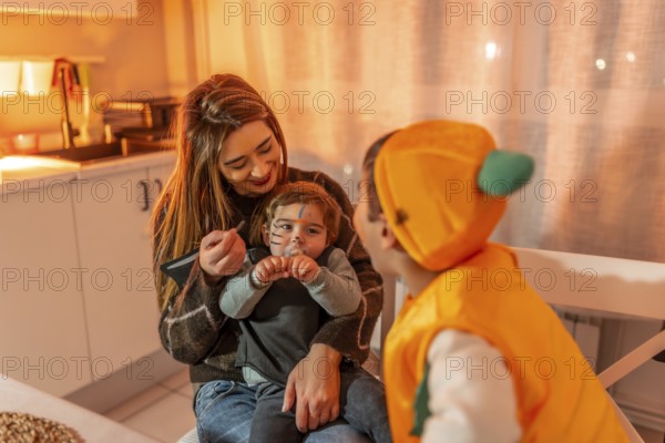 Mother applying halloween makeup on her toddler son dressed up as a cat while his brother dressed