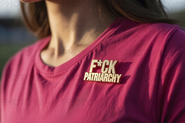 Close-up of gold pin reading FCK patriarchy on pink t-shirt. Bold feminist statement against gender