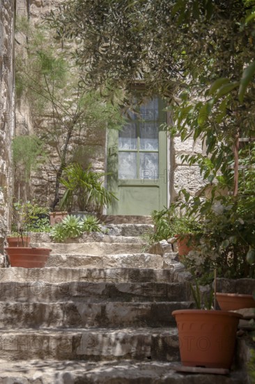 A rustic stone staircase with clay pots and green plants leads to a green door in a Mediterranean