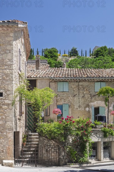 A rustic house with a terrace decorated with flowers, shutters and green hills in the background,