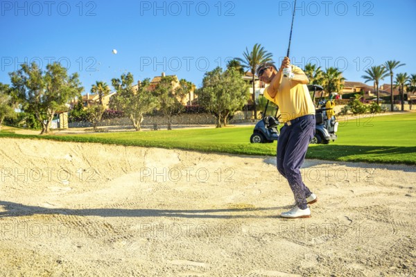 Professional golfer hitting a ball out of a sand trap on a sunny day, showcasing skill and