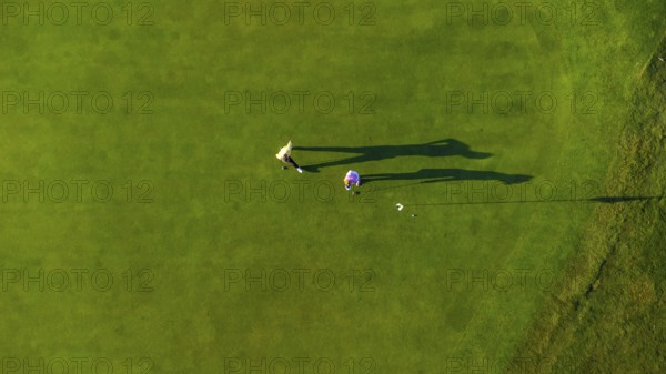 Two golfers are putting on a vibrant green golf course, seen from an aerial perspective, creating