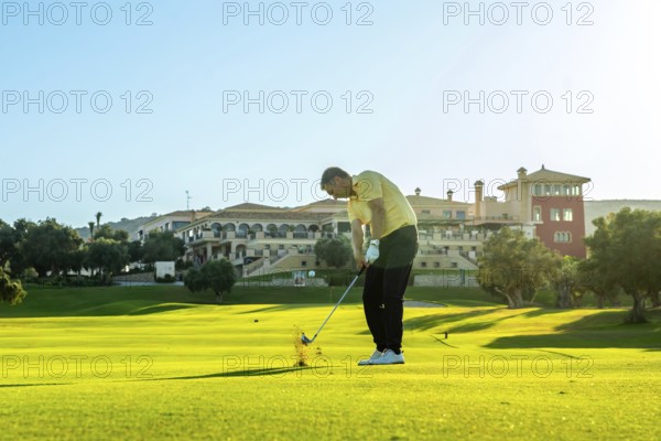 Golfer takes a swing, sending the ball flying across a vibrant green golf course, with a luxurious