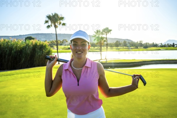Female golfer smiling while holding a golf club, posing confidently on a lush green course near a