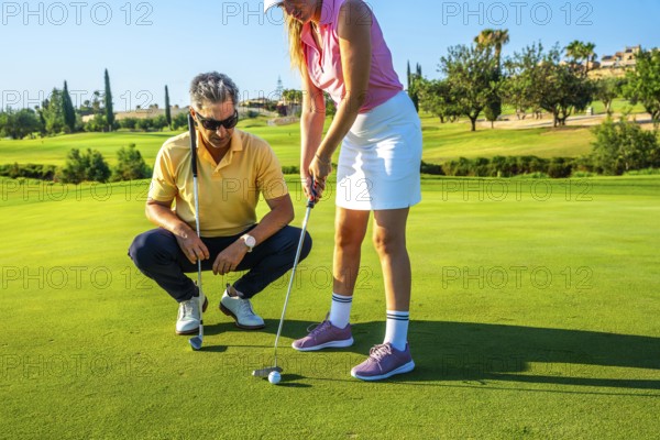Golf instructor guides a woman on putting technique on a sunny golf course. They focus on improving