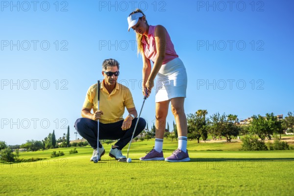 Golf instructor guides a woman on the putting green, focusing on technique under a clear blue sky.