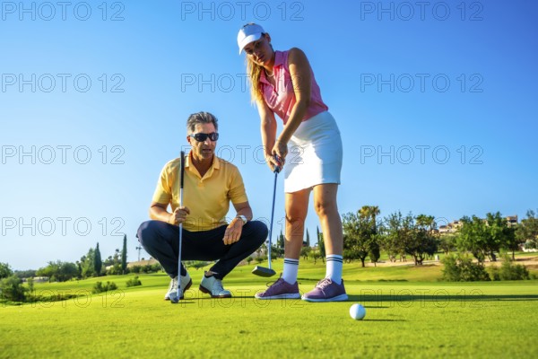 Female golfer receiving putting advice from her instructor under the warm sun, focusing on