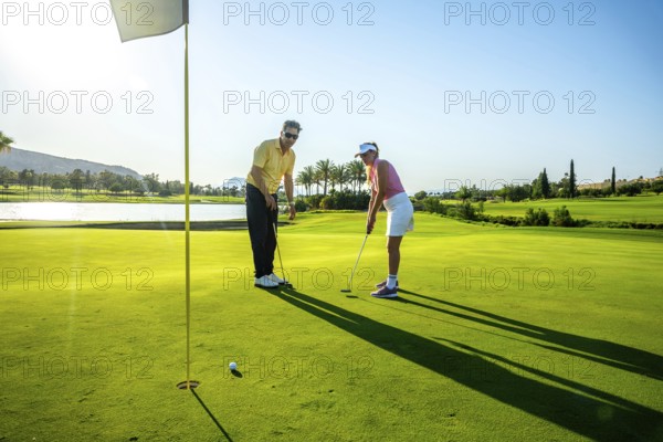 Two golfers practicing putting on a bright, sunny day at a lush golf course, surrounded by palm