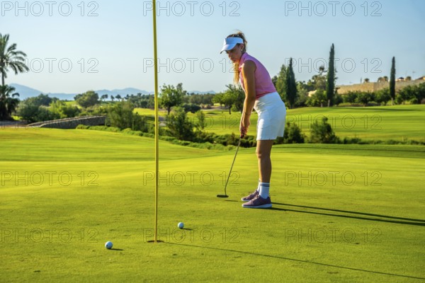 Professional golfer concentrating on putting the ball into the hole on a sunny day at the golf