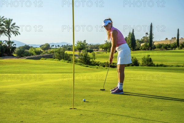 Professional golfer putting the ball on a lush green course under a bright sun, showcasing skill
