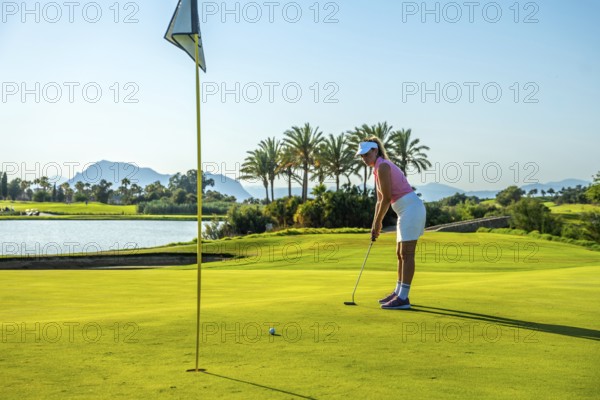 Woman golfer concentrating on putting on the green of a beautiful golf course with palm trees, a