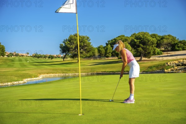 Female golfer concentrating on putting the ball on a sunlit day, enjoying the beauty of a lush golf
