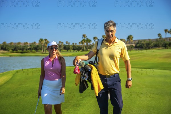 Couple enjoying a sunny day playing golf, walking on a beautiful green golf course, carrying golf