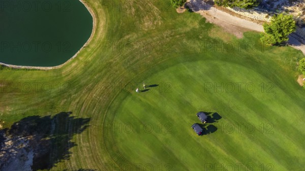 Scenic aerial view of a golf course featuring two players walking near golf carts on a lush green