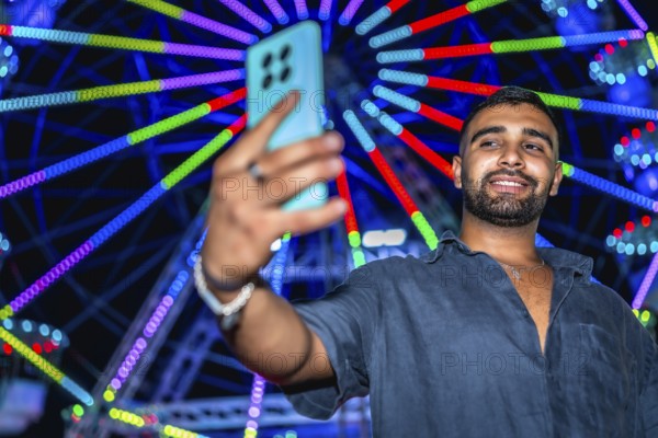 Tourist taking selfie with smartphone in front of illuminated ferris wheel at amusement park,