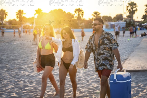 Three friends walking on the beach at sunset, one of them pointing towards something while another