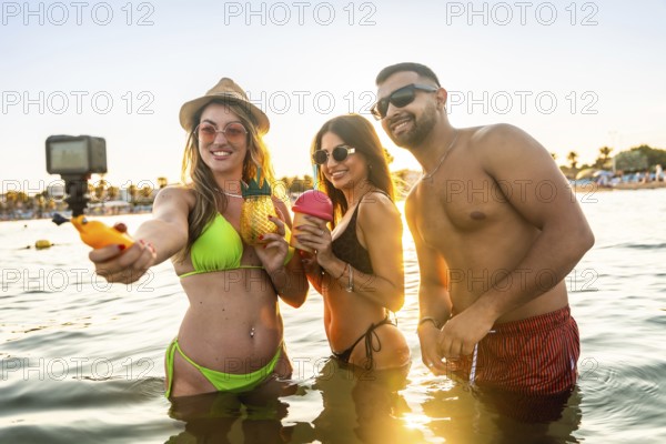Young tourists capturing a joyful selfie in the sea during a vibrant sunset, celebrating summer