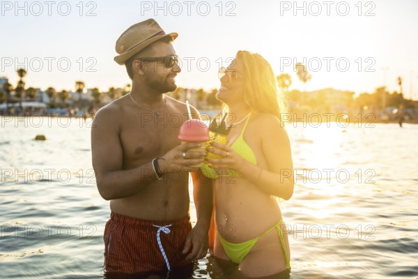 Tourists enjoying cocktails while wading in the ocean at sunset, embracing the warmth of summer and