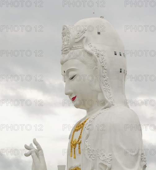 Majestic white guan yin statue, a prominent buddhist figure, stands tall against a cloudy sky in