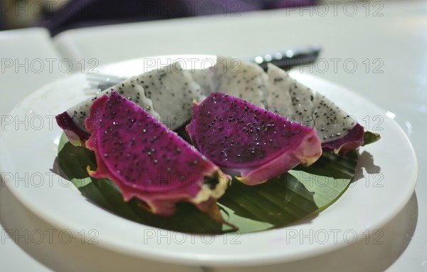 Vibrant slices of red and white dragon fruit are presented on a banana leaf atop a white plate,