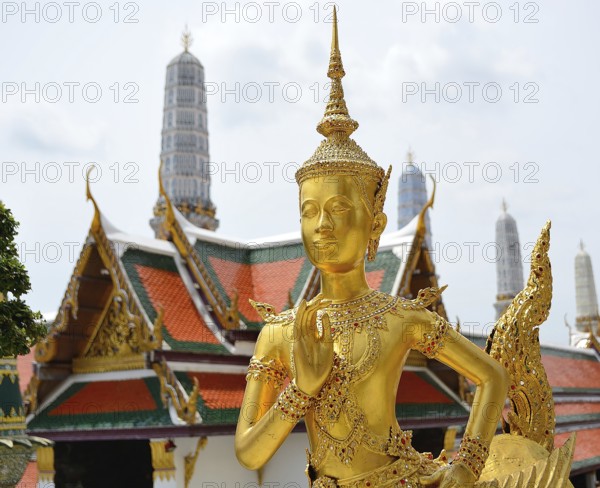 Golden kinnara statue praying with hands joined in a traditional thai greeting, inside the wat phra