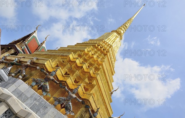 Golden chedi reaching for a bright blue sky, supported by decorative figures, within the majestic