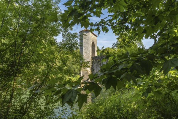 Green leaves frame a medieval bridge tower in sauveterre de bearn, france, creating a picturesque