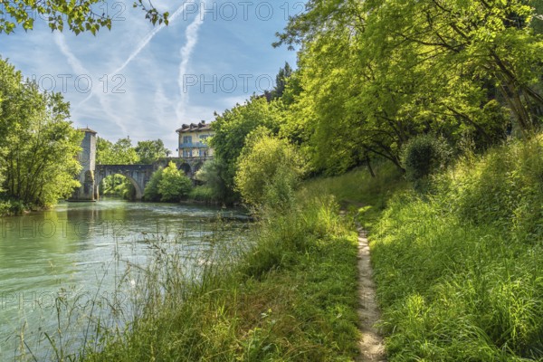 Lush vegetation frames a tranquil pathway meandering along the gave d'oloron river, leading towards