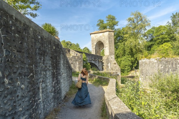 Tourist walking on a sunny day towards the medieval bridge of sauveterre de bearn in france,