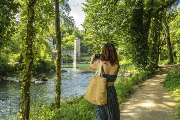 Tourist photographing the gave d'oloron river and its fortified bridge in sauveterre de bearn, a