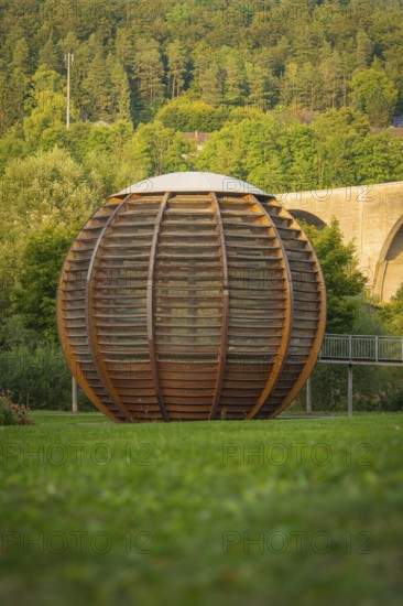 Large wooden ball in a park, surrounded by green grass and trees in the background, Nagold,