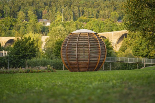 Large wooden ball in front of a bridge, surrounded by green trees and grassland, Nagold, district